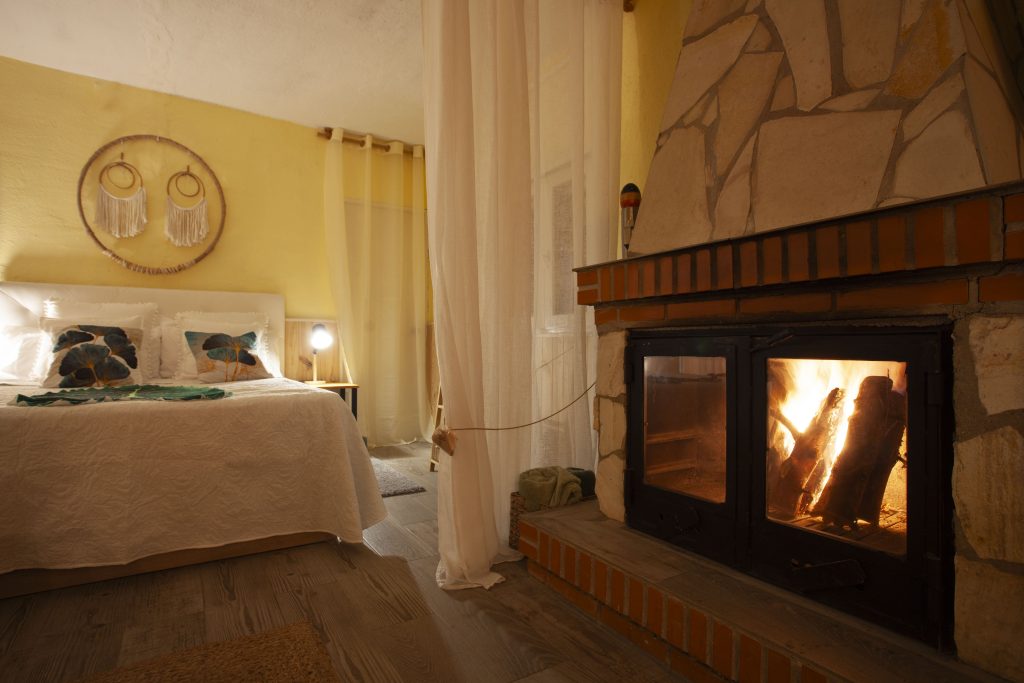 Interior de la casita de La Finquita con chimenea encendida y cama de matrimonio en Lupiana